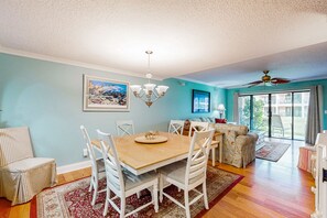 A dining area with a wooden table and white chairs, a chandelier, and a painting on the wall. - Patio Condo in Oceanfront Community w/ Pool Walk to Beach (St. Augustine)