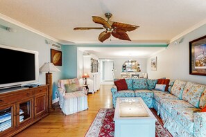 A living room with a large flat-screen TV, a ceiling fan, a sofa, a coffee table, and a patterned rug. - Patio Condo in Oceanfront Community w/ Pool Walk to Beach (St. Augustine)