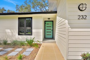 Una casa moderna con una porta verde, il numero 232 e una piccola finestra.