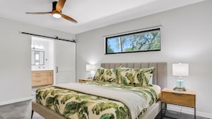 A bedroom with a bed, a ceiling fan, a nightstand, a window, and a door leading to another room. - Renovated Home With Private Pool, Patio, Outdoor Fireplace, & Grill (St. Augustine)