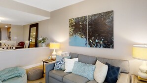 A living room with a grey sofa, a blue bean bag, and a wall-mounted painting. - Sea Marsh Retreat Condo in Fernandina Beach in a Gated Community (Fernandina Beach)