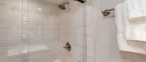 A modern shower with a glass door, a handheld showerhead, and a towel rack with folded towels.