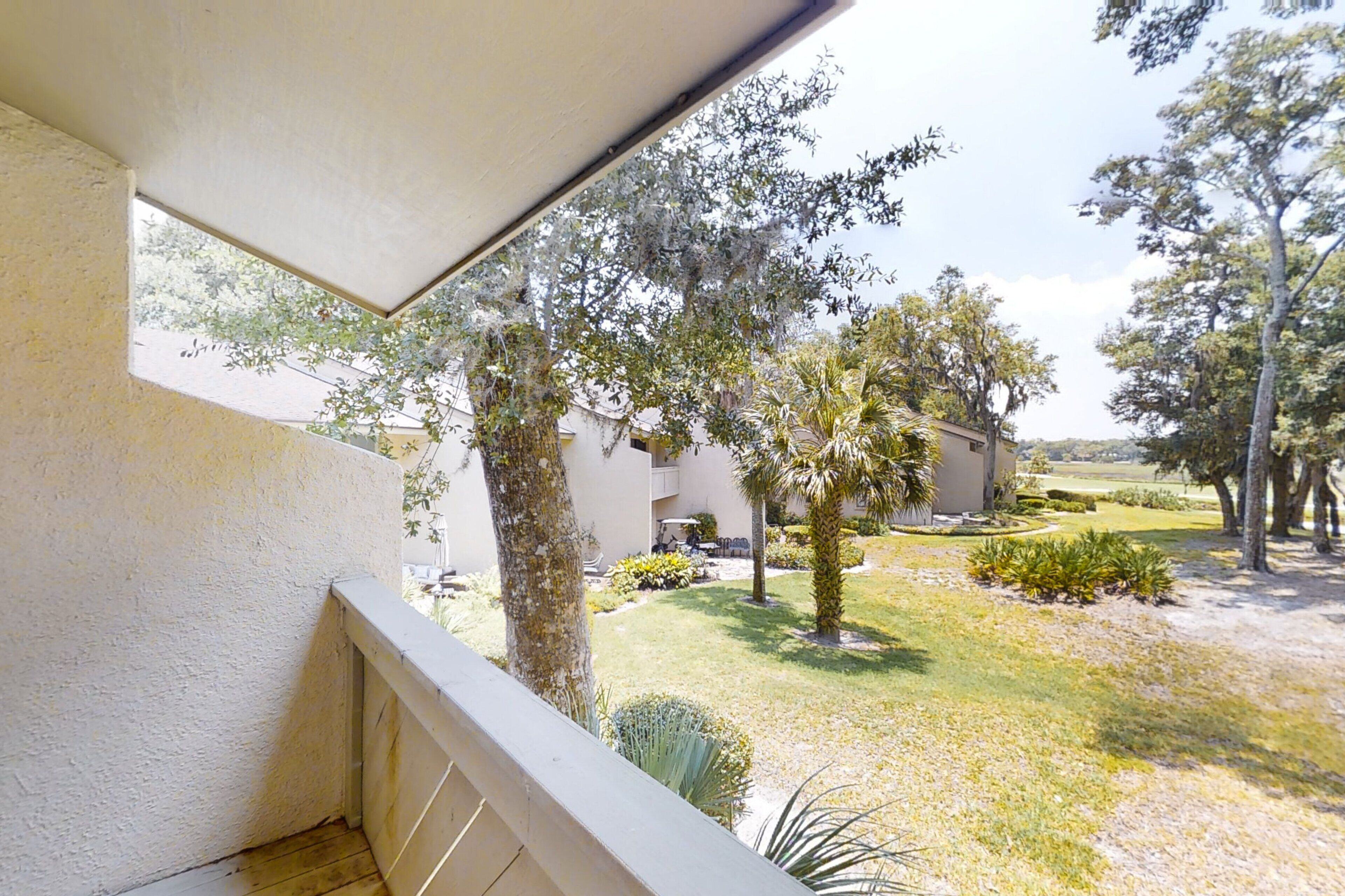 A balcony with a view of a landscaped garden, including trees and a lawn.