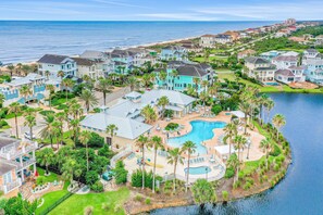 A coastal residential area with houses, a large swimming pool, and a beach in the background. - Spacious Fourth-floor Beachfront Condo With Pools, hot Tub, Fitness Room (Palm Coast)
