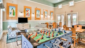 Ett rum med ett bordfotbollsspel, en tv, mönstrade soffor, ett matbord och konstverk på väggarna.