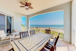 A covered outdoor dining area with a view of the ocean, a ceiling fan, and a table with chairs. - Spacious Fourth-floor Beachfront Condo With Pools, hot Tub, Fitness Room (Palm Coast)