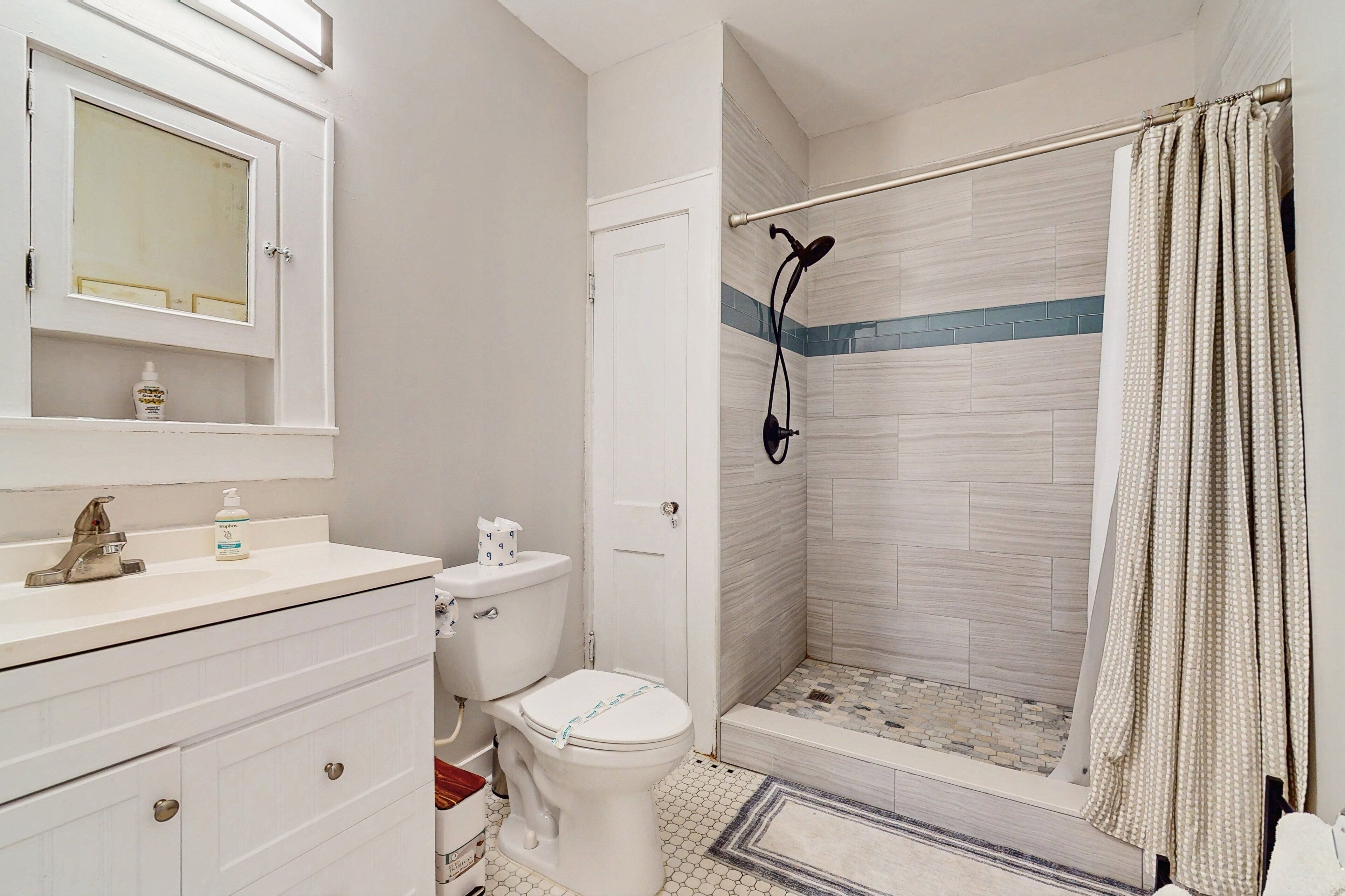 A bathroom with a toilet, sink, mirror, and shower.