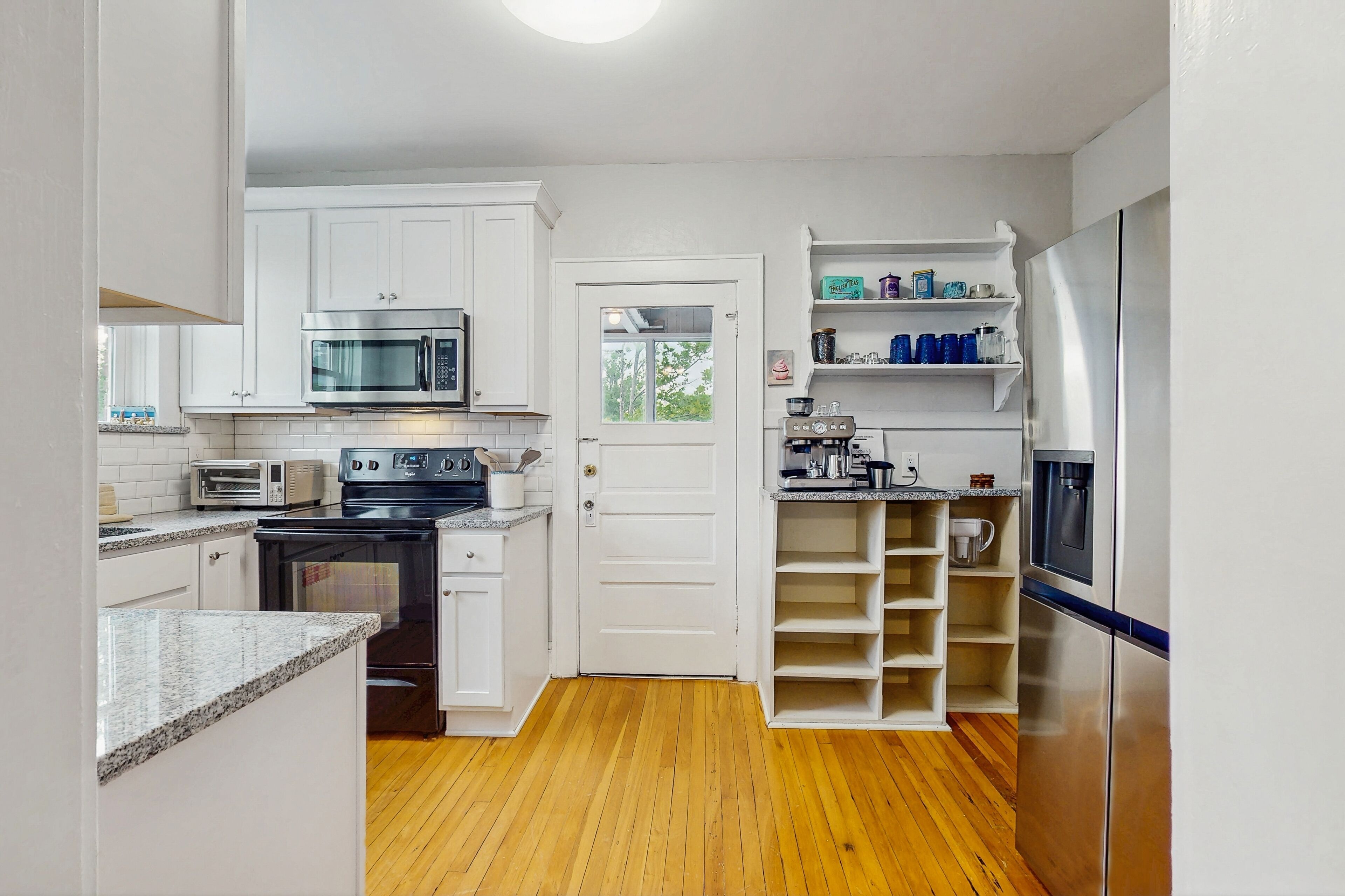 A compact kitchen with white cabinets, a microwave, a stove, a refrigerator, and a water dispenser.
