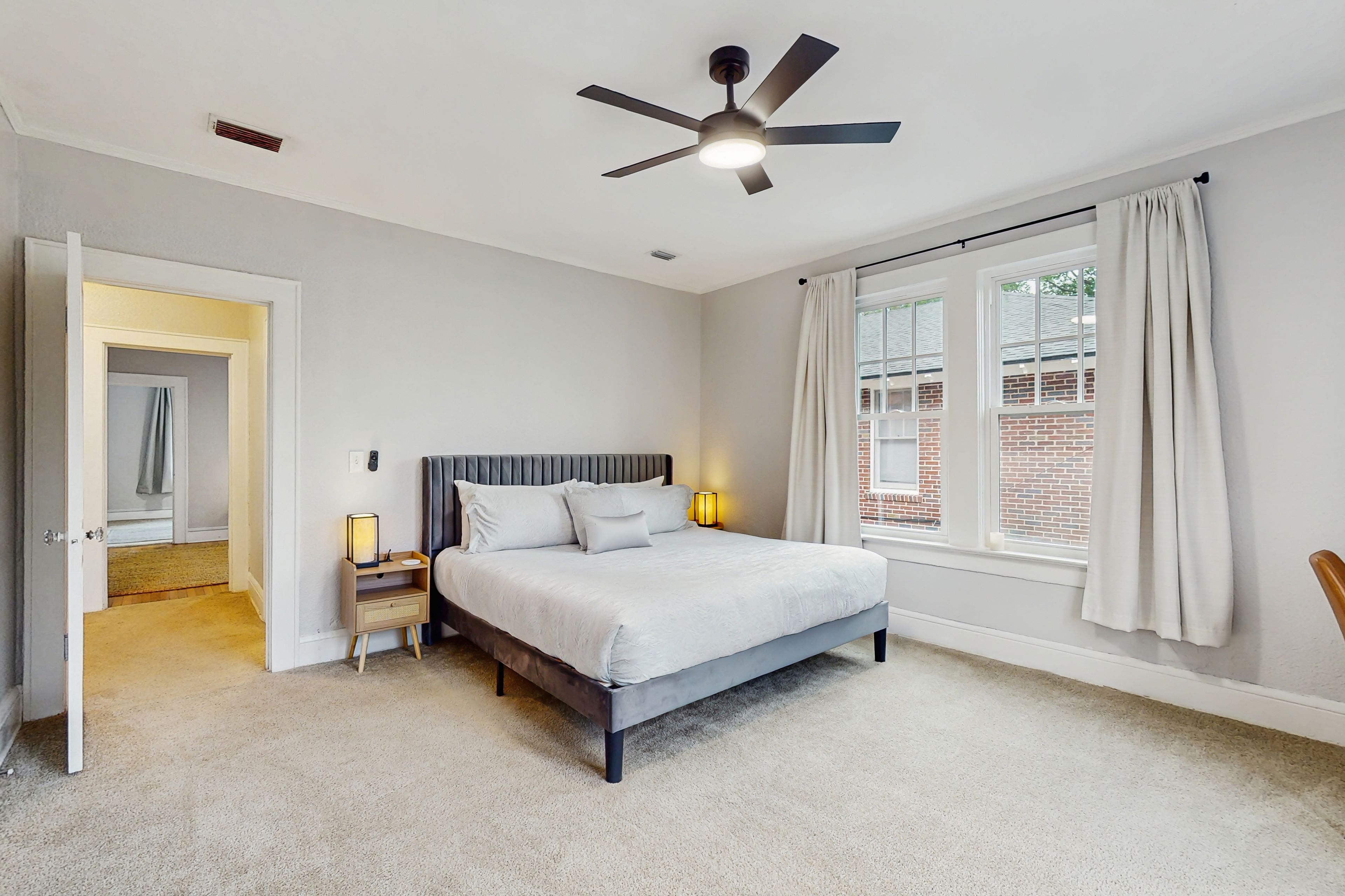 A bedroom with a bed, bedside lamps, a ceiling fan, and a window with curtains.