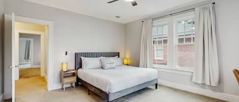 A bedroom with a bed, bedside lamps, a ceiling fan, and a window with curtains.