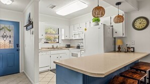 A kitchen with white cabinets, a large island with stools, a blue door, and a wall clock. - Snowbird-friendly Condo With Patio, Central AC, W/d, Pool & Tennis - Near Beach (St. Simons Island)