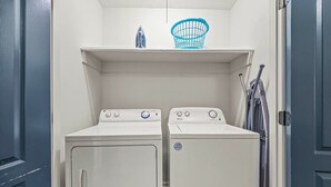 A laundry room with two front-loading washing machines and a blue laundry basket on a shelf. - Snowbird-friendly Condo With Patio, Central AC, W/d, Pool & Tennis - Near Beach (St. Simons Island)