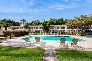 A pool area with lounge chairs, a table, and a view of apartment buildings. - Snowbird-friendly Condo With Patio, Central AC, W/d, Pool & Tennis - Near Beach (St. Simons Island)