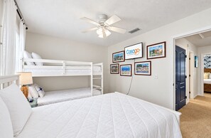 A bedroom with a bunk bed, a single bed, a ceiling fan, and a wall-mounted TV displaying the 'Casago' brand. - Snowbird-friendly Condo With Patio, Central AC, W/d, Pool & Tennis - Near Beach (St. Simons Island)