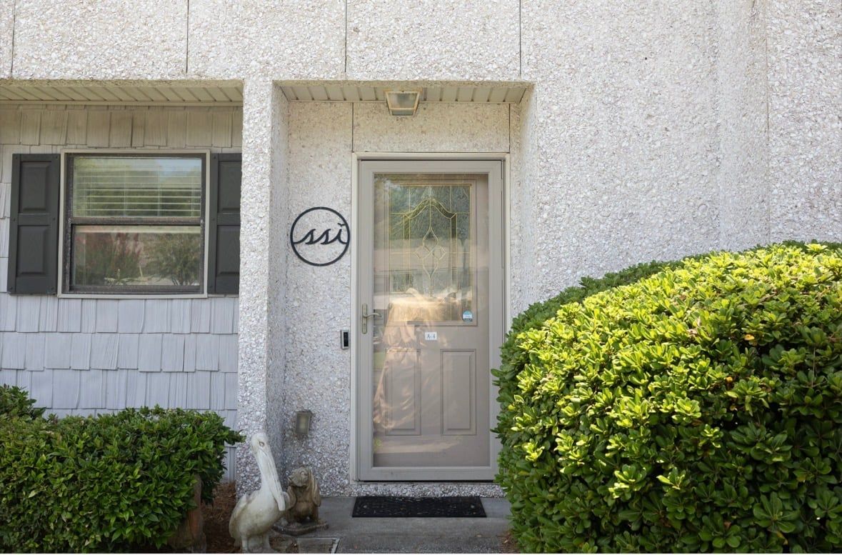 A building facade with a textured exterior, a door with a glass panel, and a small circular logo above the door.