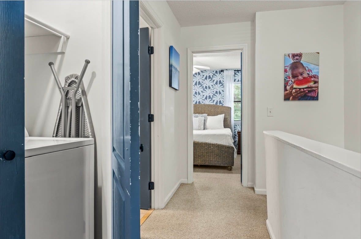 A hallway leading to a bedroom with a bed, a wall-mounted picture, and a door with a towel rack.