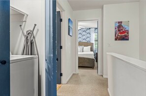 A hallway leading to a bedroom with a bed, a wall-mounted picture, and a door with a towel rack. - Snowbird-friendly Condo With Patio, Central AC, W/d, Pool & Tennis - Near Beach (St. Simons Island)