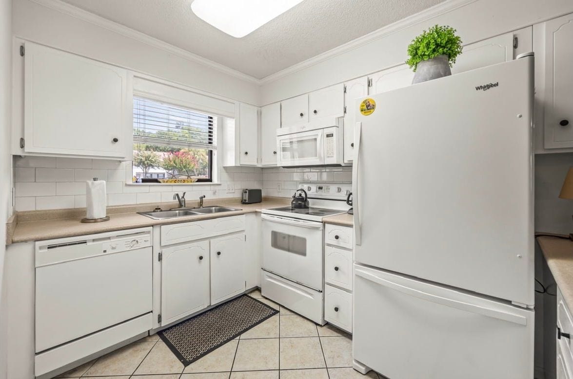 A kitchen with white cabinetry, a built-in microwave, a refrigerator, and a window with a view of trees.