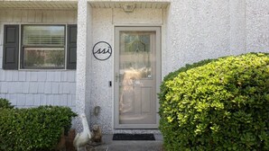 A building facade with a textured exterior, a door with a glass panel, and a small circular logo above the door. - Snowbird-friendly Condo With Patio, Central AC, W/d, Pool & Tennis - Near Beach (St. Simons Island)