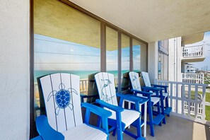 Ein Balkon mit blauen und weißen Adirondack-Stühlen, einem weißen Geländer und Blick auf das Meer und Gebäude.