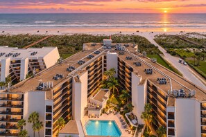 Un hotel con varios pisos, una piscina en la azotea y vistas a la playa y el océano al atardecer.