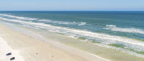 A wide sandy beach with gentle waves and a clear sky.