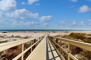 Une promenade en bois menant à une plage, avec un ciel dégagé.
