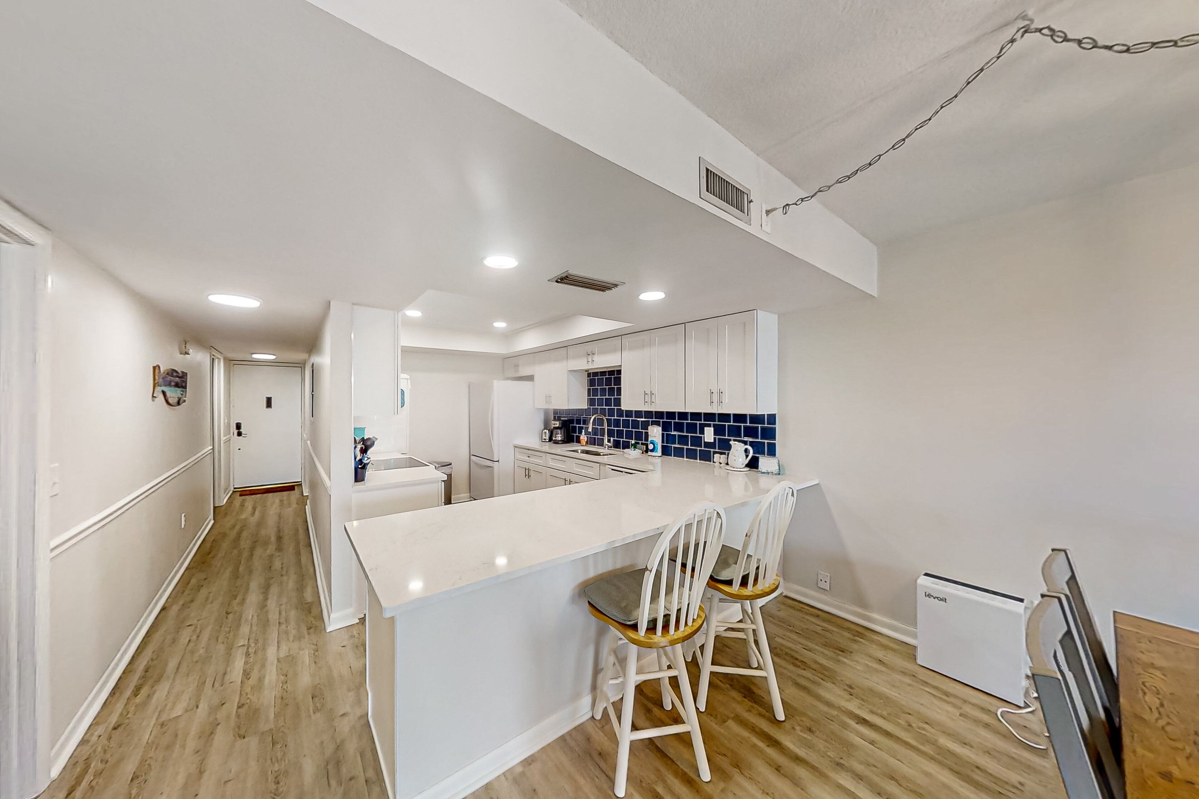 Una cocina moderna con armarios blancos, una isla central con dos sillas y un refrigerador pequeño.