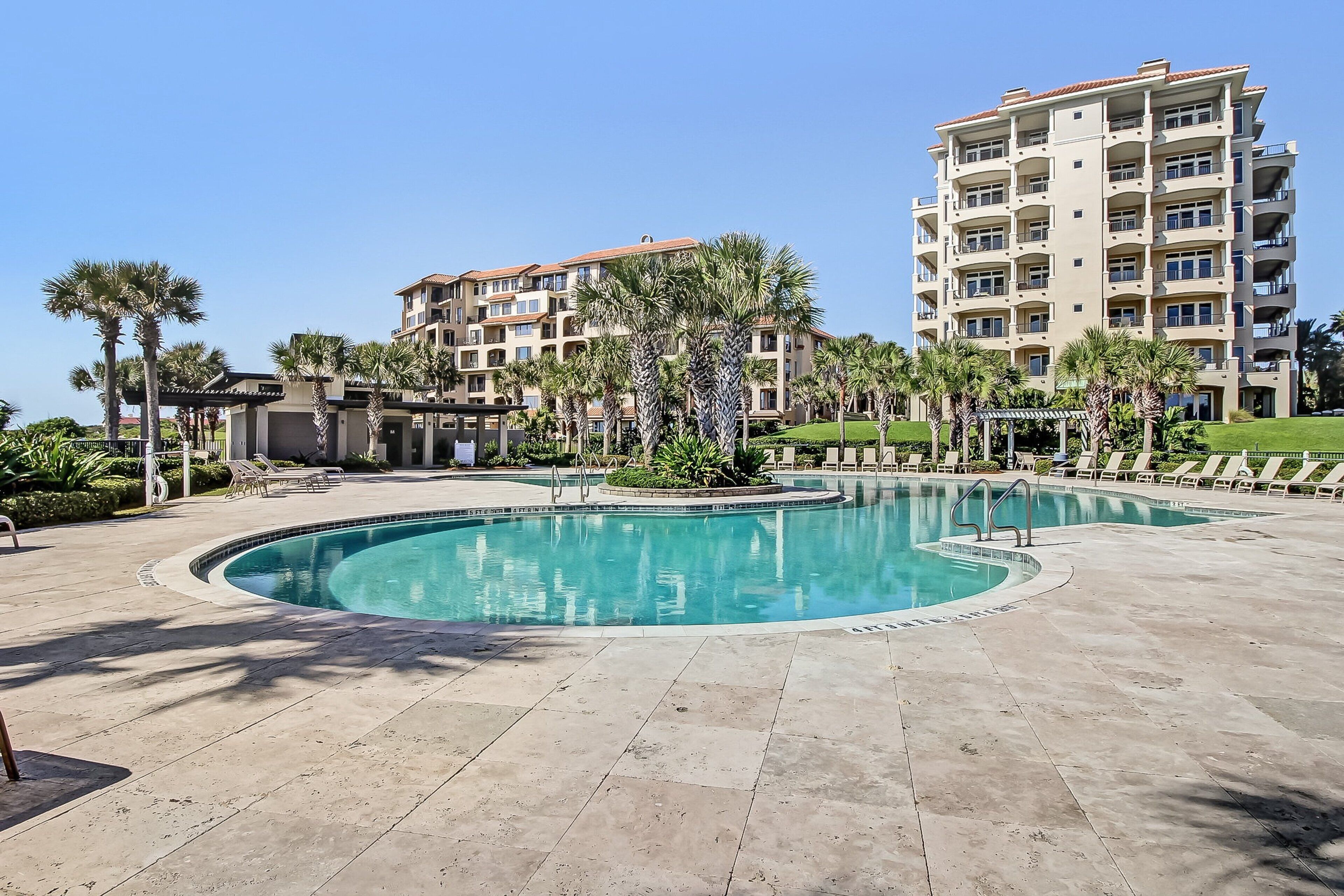 A hotel with a swimming pool, palm trees, and a well-maintained lawn.