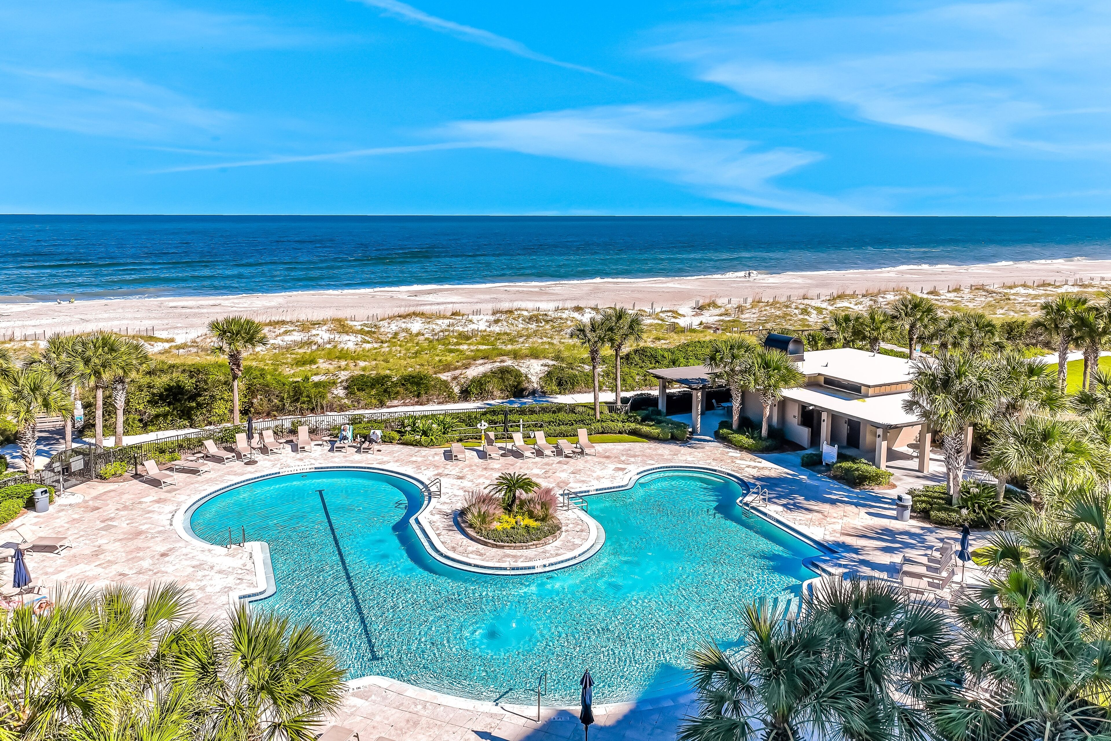 A resort with a swimming pool, beach view, and palm trees.