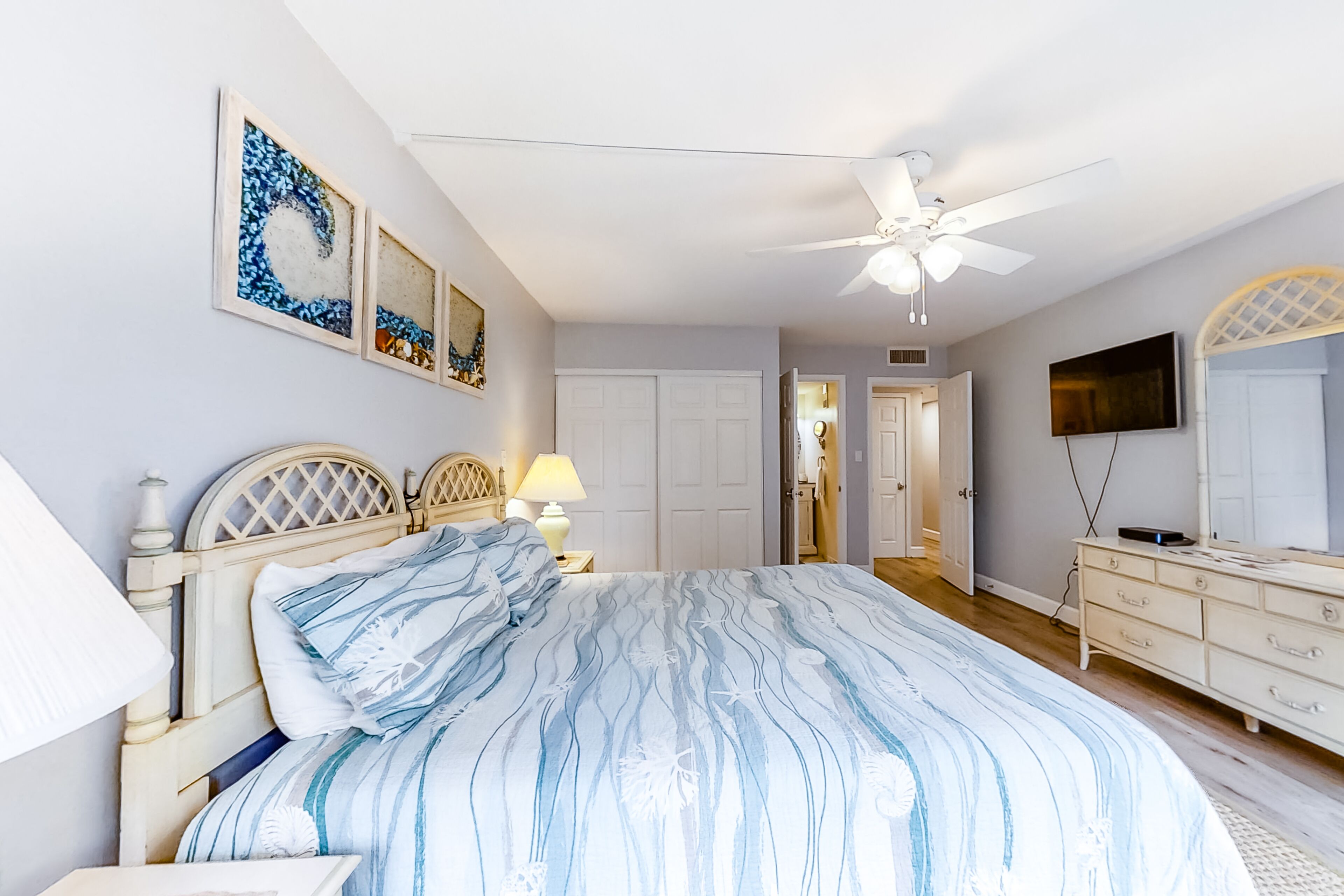 A bedroom with a bed, a dresser, a TV, and artwork on the wall.