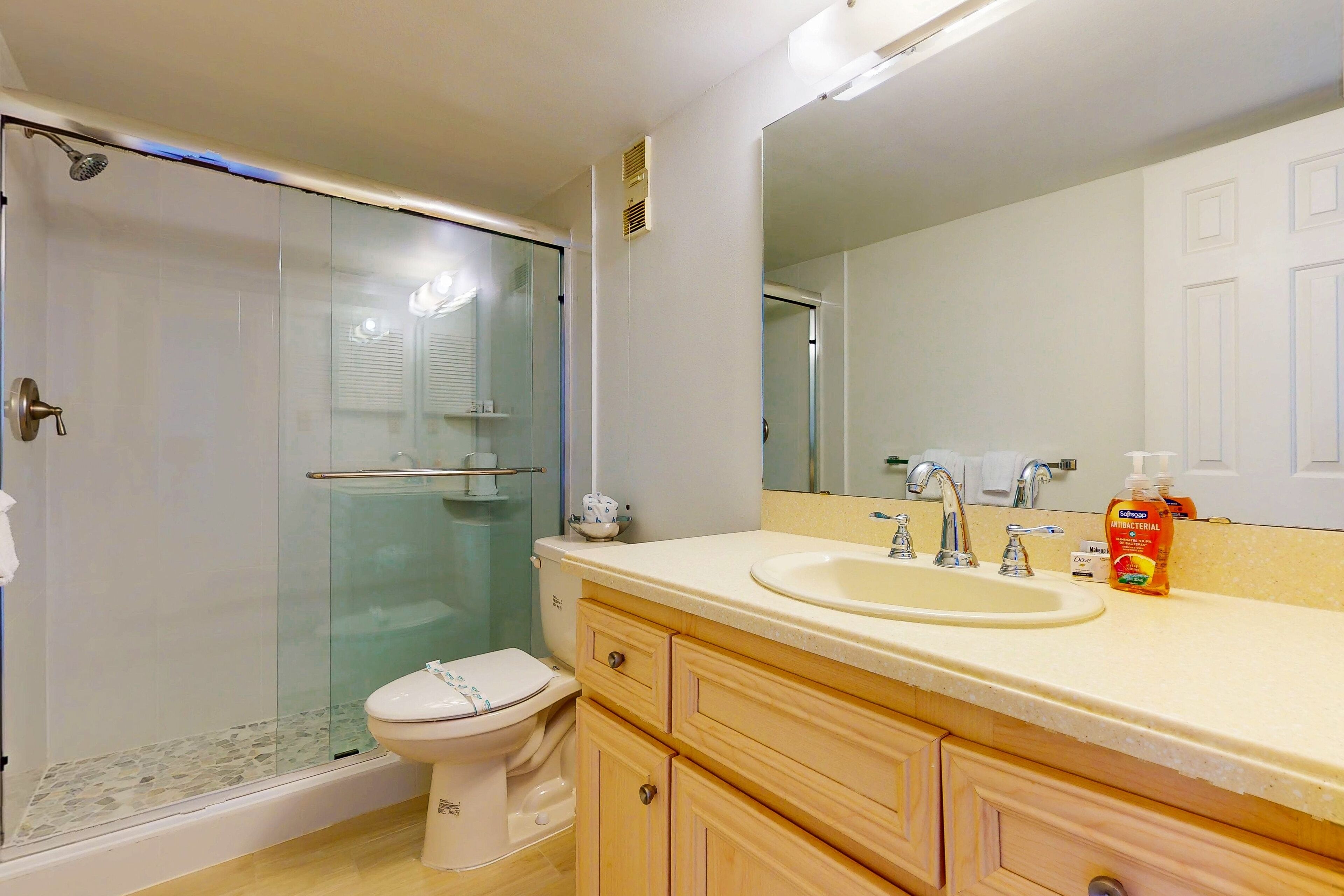 A bathroom with a glass-enclosed shower, a toilet, a sink with a mirror, and wooden cabinets.