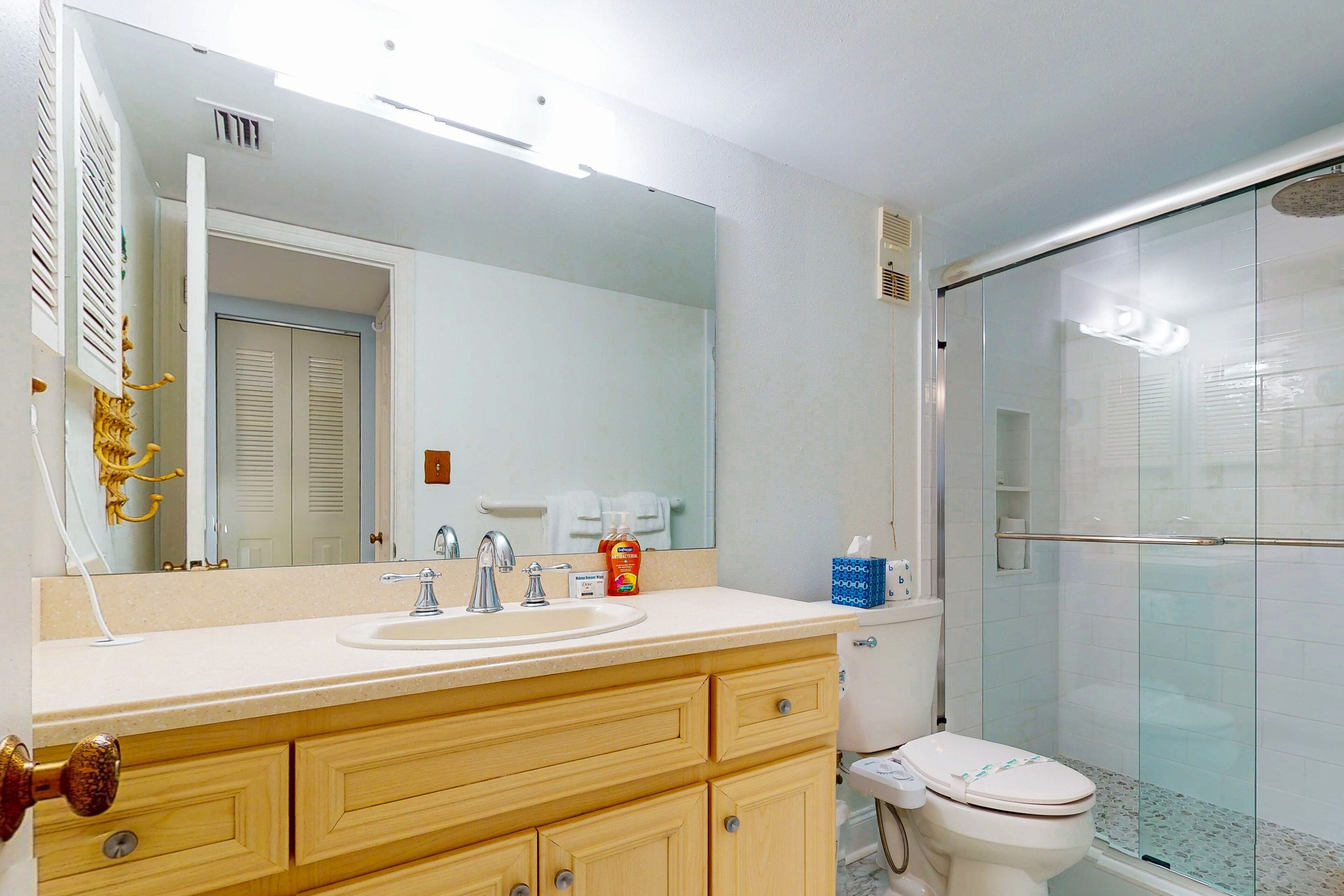 A bathroom with a sink, mirror, toilet, and glass shower enclosure.