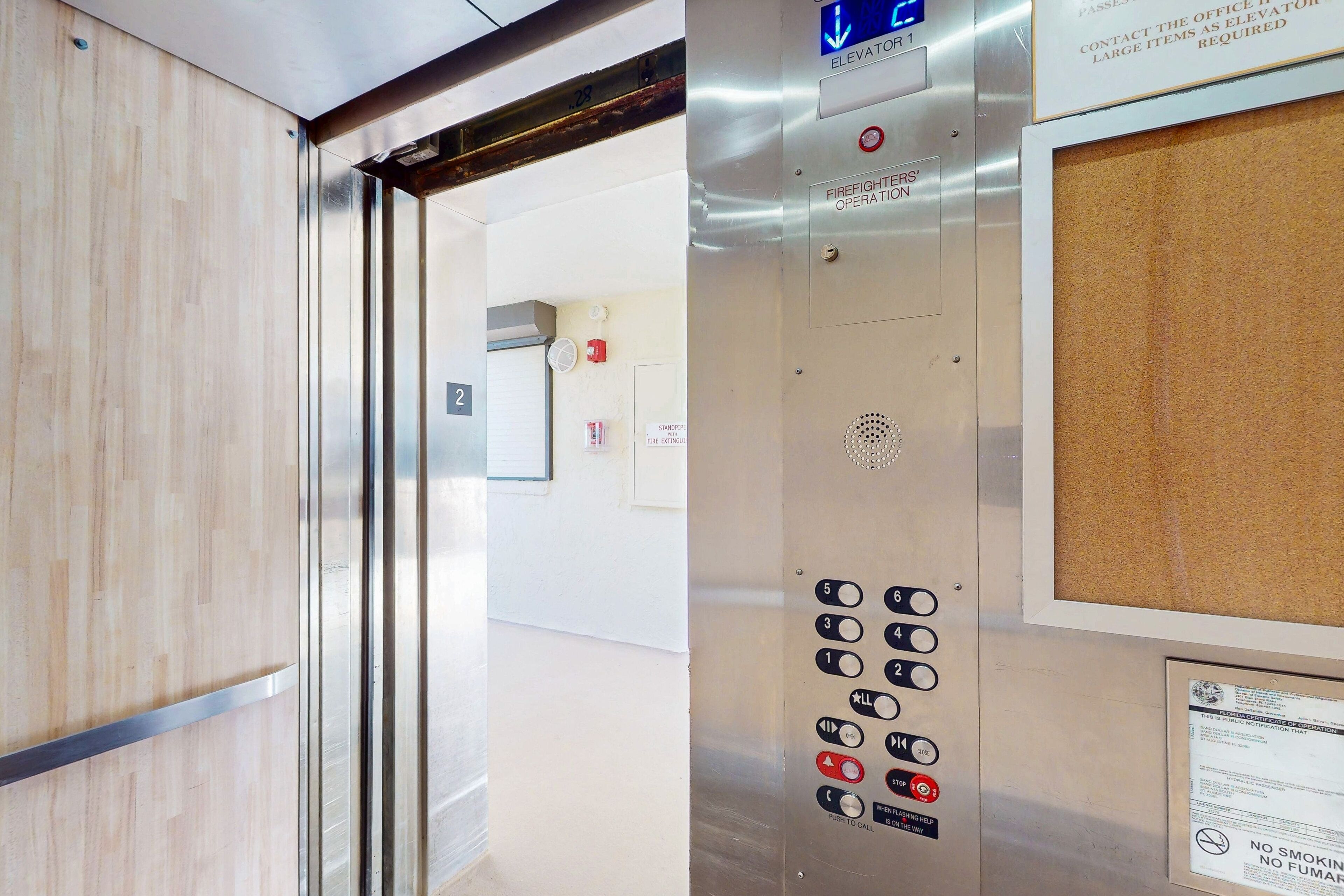 Een liftinterieur met een bedieningspaneel, noodknoppen en een bord met een vluchtweg.