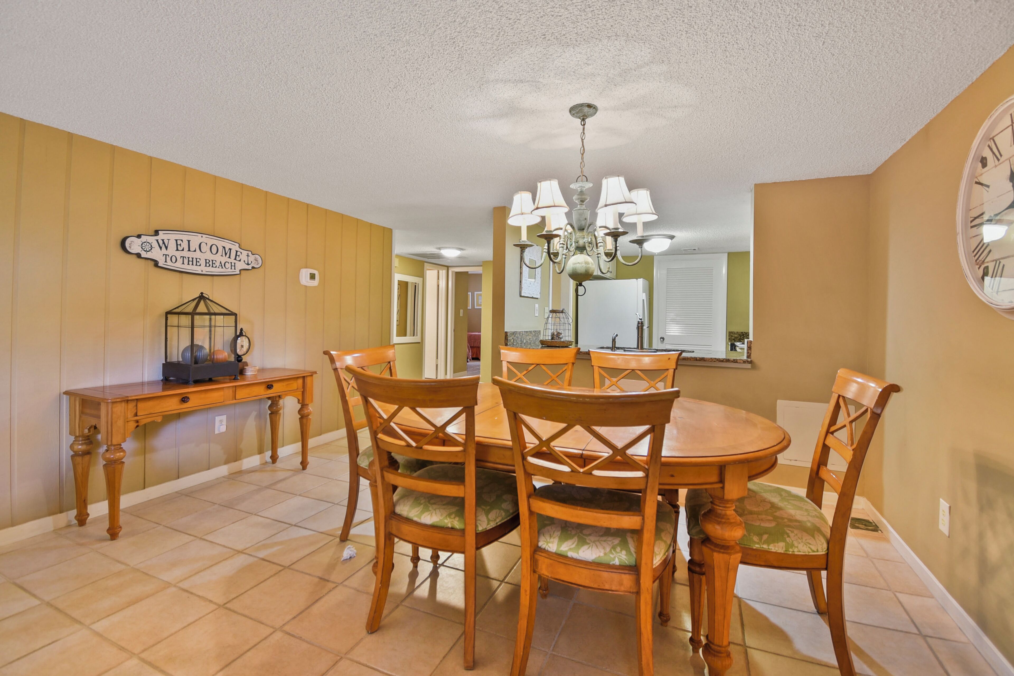 A dining area with a wooden table and chairs, a chandelier, and a 'Welcome to the Beach' sign.