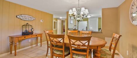 A dining area with a wooden table and chairs, a chandelier, and a 'Welcome to the Beach' sign.
