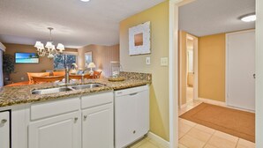 A kitchen with white cabinets, granite countertops, and a dishwasher. There is a dining area with orange chairs and a table. - Relaxing Amelia Island Retreat 2br/2ba Condo in Amelia Island Plantation (Fernandina Beach)
