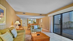 A spacious living room with a green sofa, a wooden coffee table, and a dining area in the background. - Relaxing Amelia Island Retreat 2br/2ba Condo in Amelia Island Plantation (Fernandina Beach)