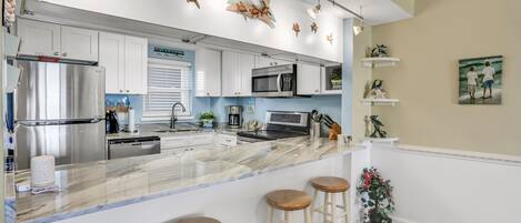 A kitchen with white cabinets, a stainless steel refrigerator, a microwave, and a coffee maker. There are two wooden stools at the island.