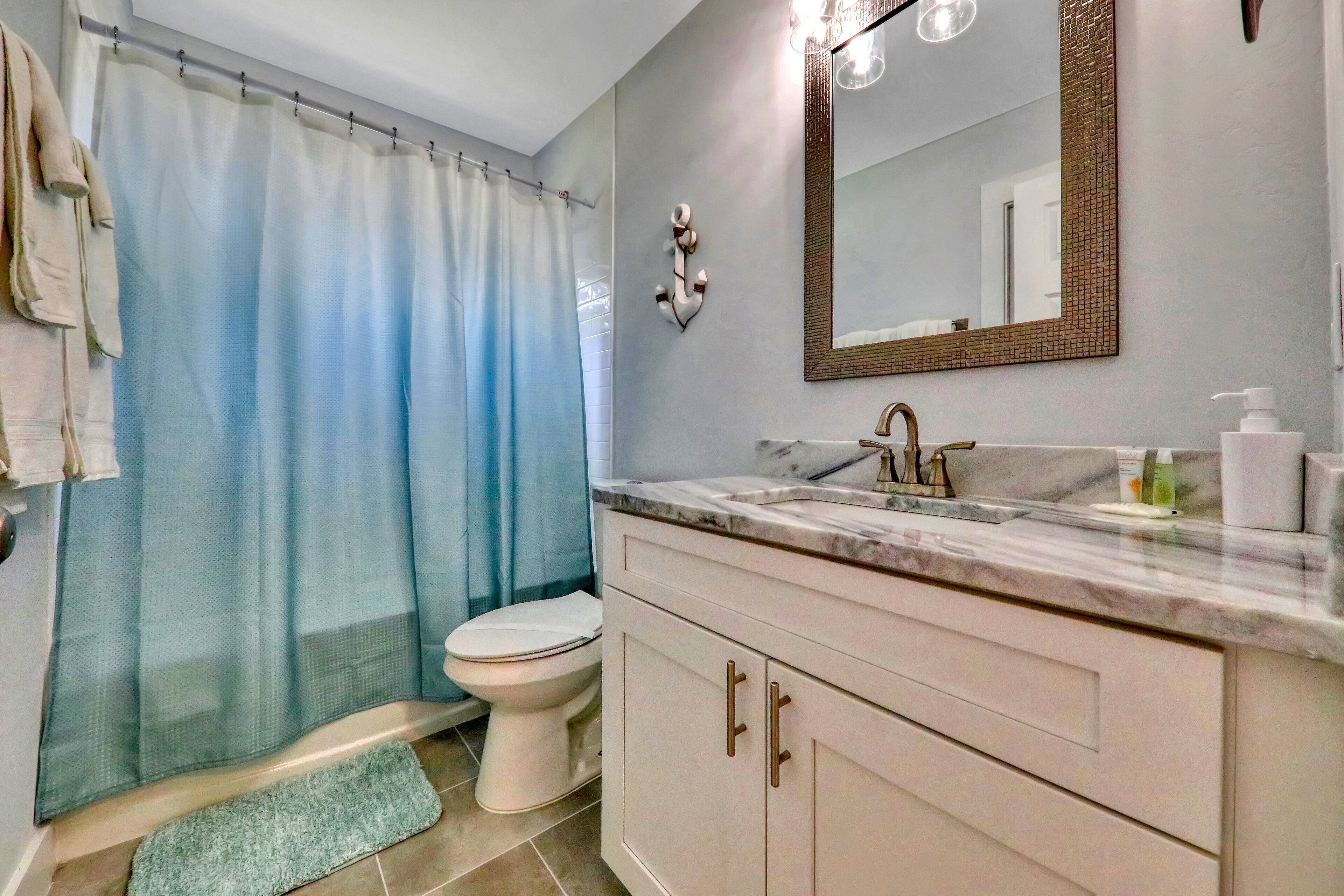 A bathroom with a shower curtain, a toilet, a sink with a mirror, and a mat on the floor.