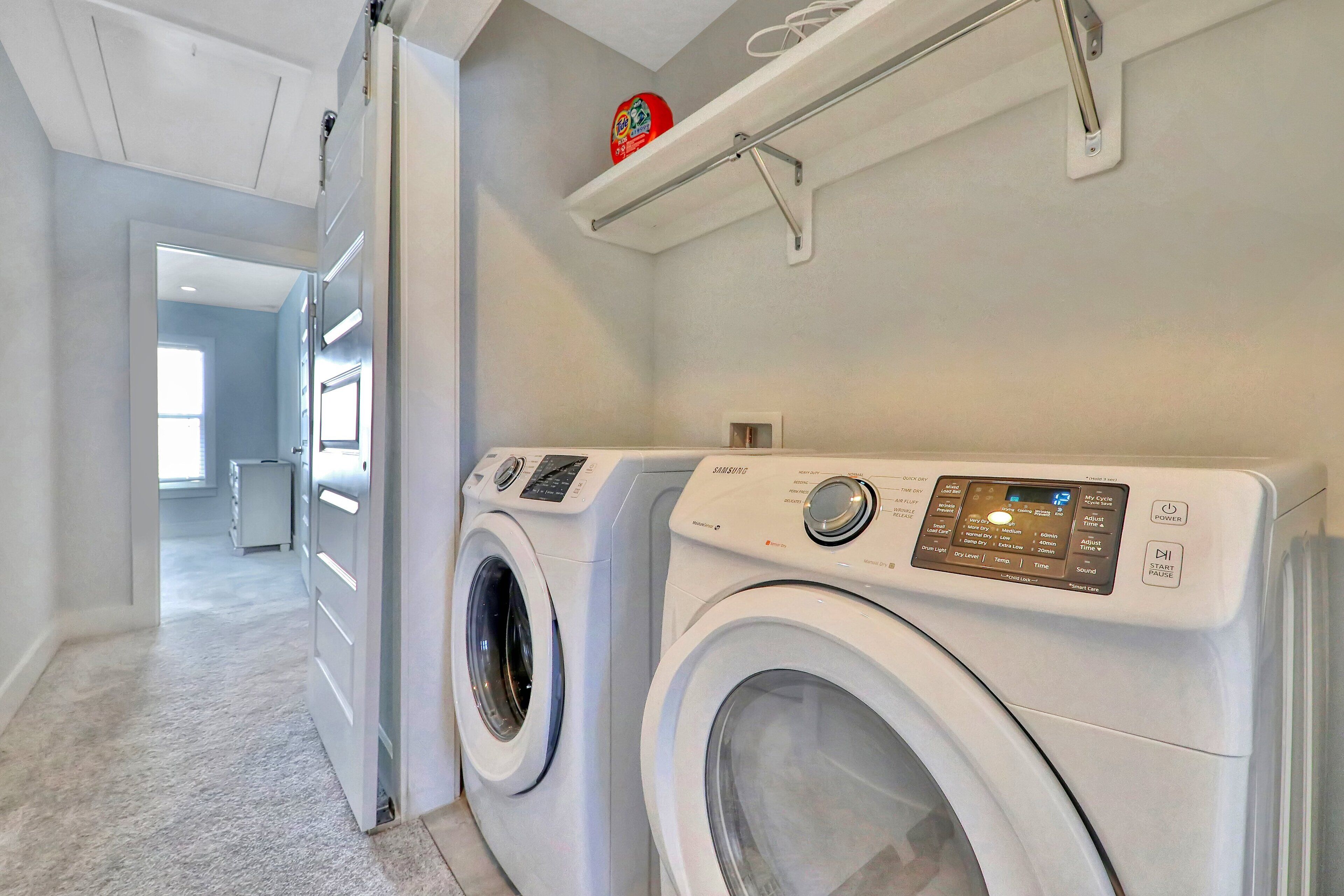 A laundry room with two front-loading washing machines and a shelf above.