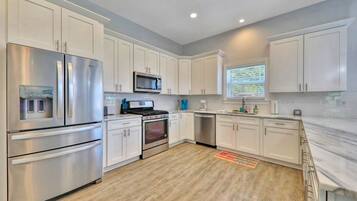 A modern kitchen with white cabinets, stainless steel appliances, and a wooden floor.