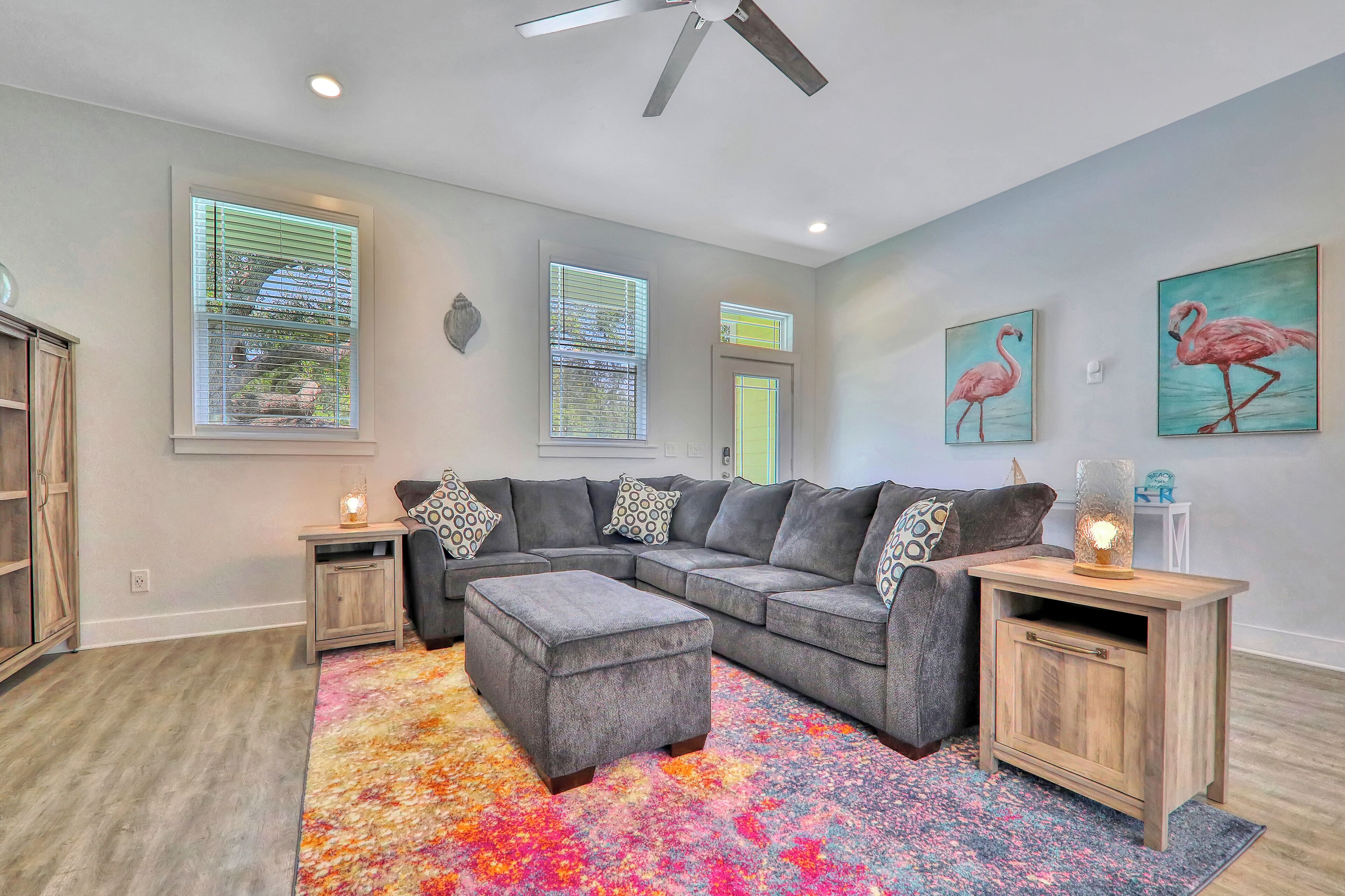 A living room with a sectional sofa, ottoman, wooden side tables, and a colorful rug.