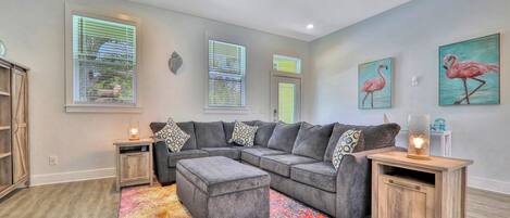 A living room with a sectional sofa, ottoman, wooden side tables, and a colorful rug.