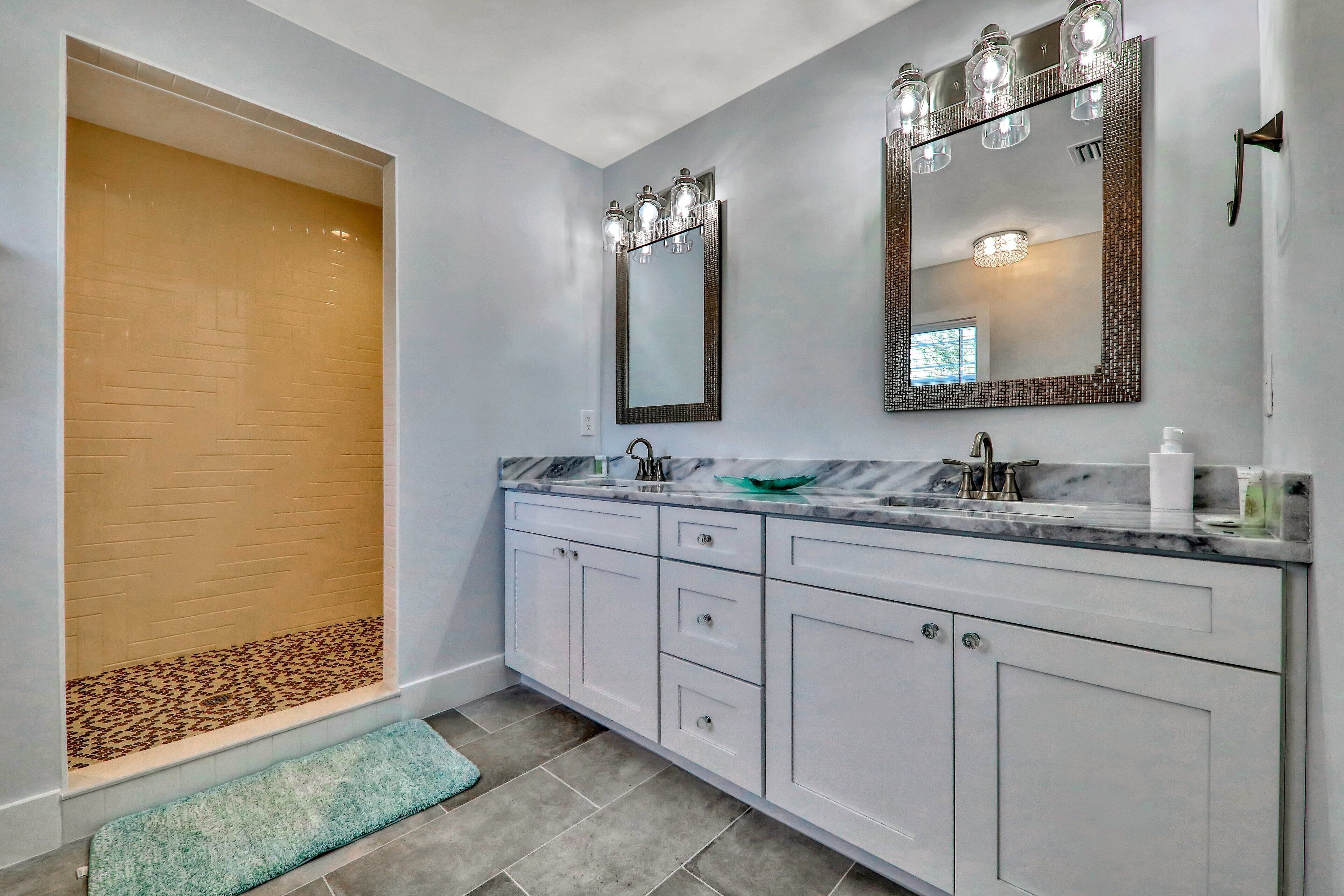 A bathroom with a walk-in shower, a large mirror, and a marble countertop.
