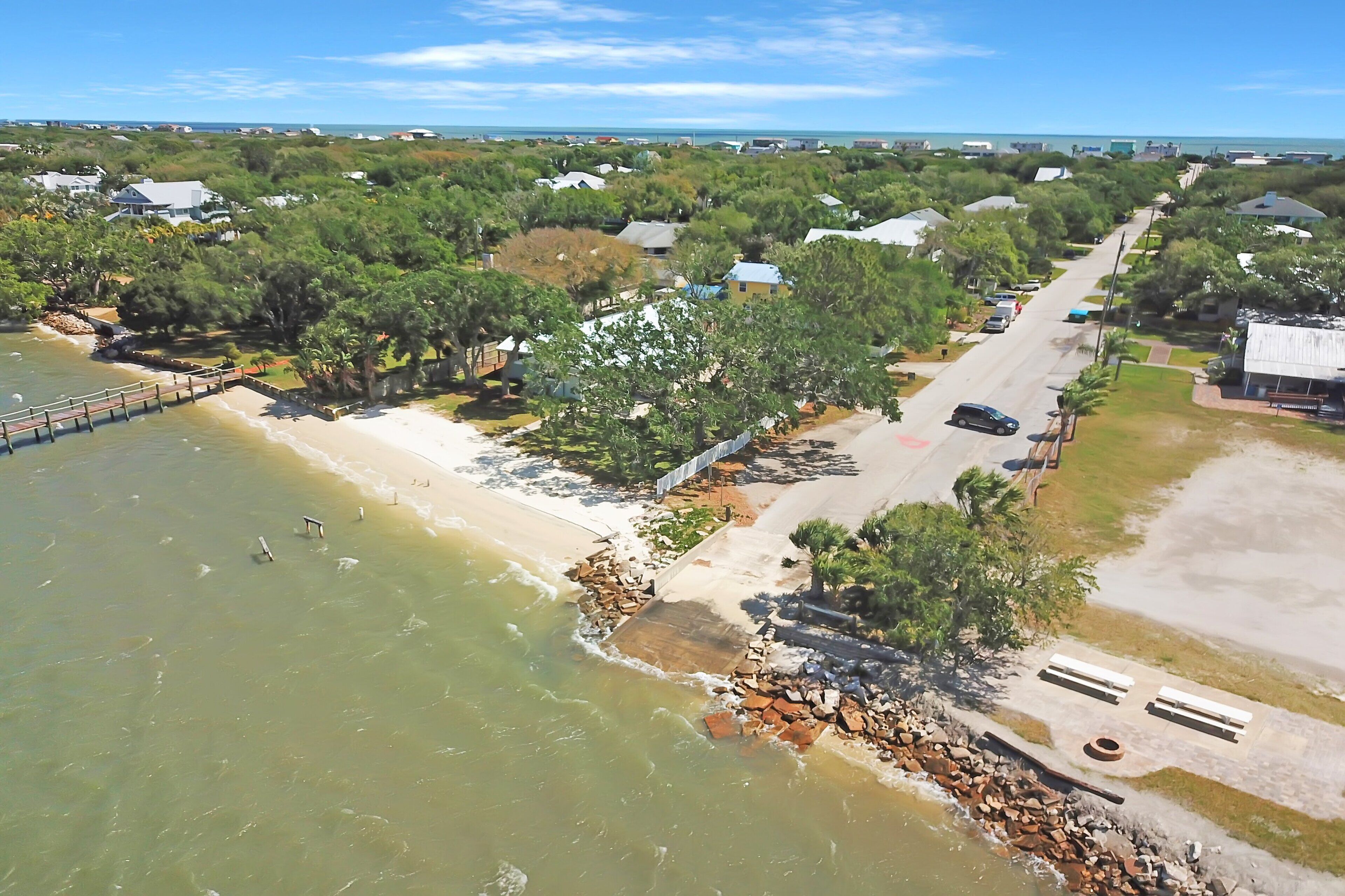 Vista aérea de uma área residencial costeira com casas, uma praia e um cais.
