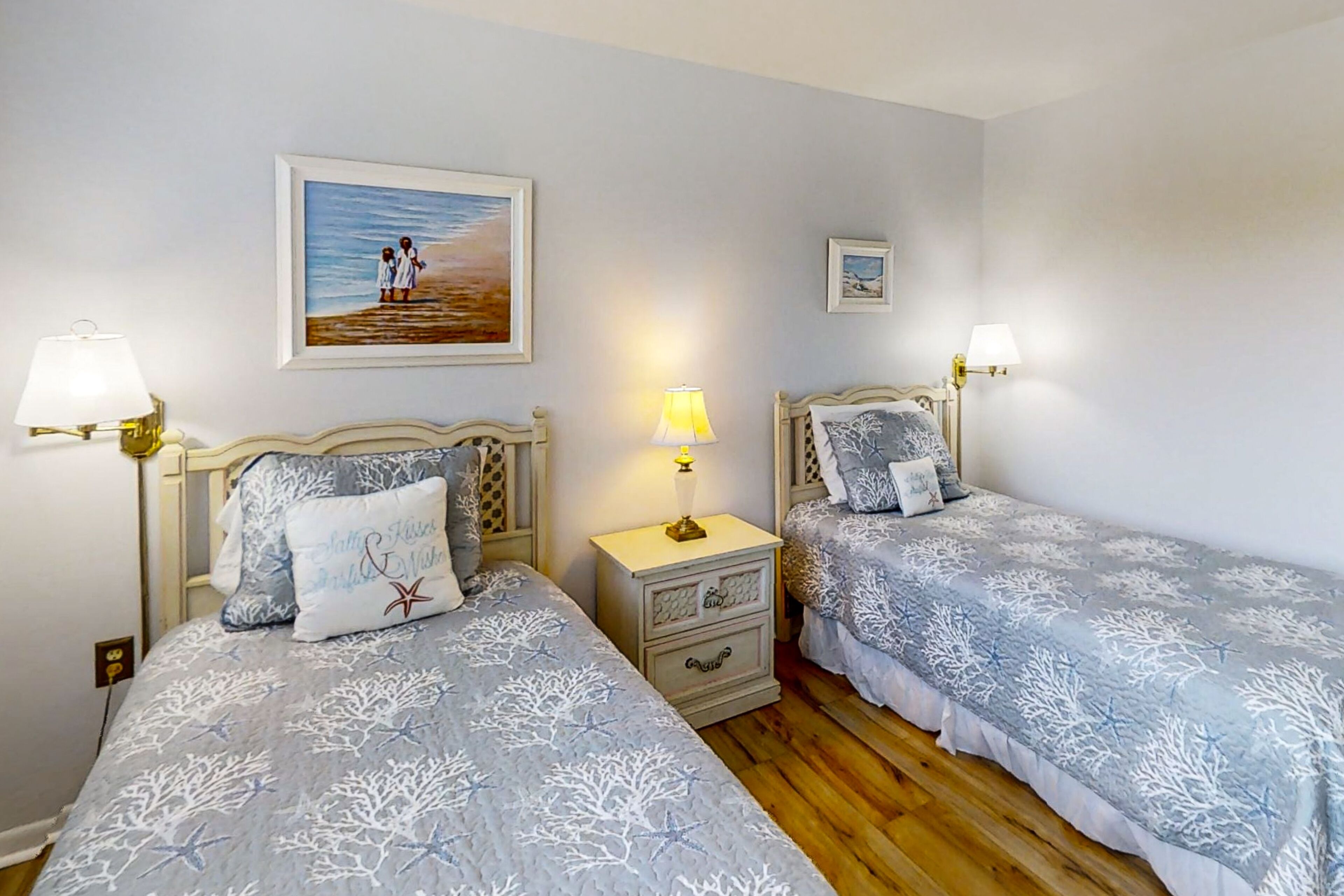 Une chambre à coucher avec deux lits, chacun doté d’une tête de lit et de tables de chevet assorties. Un tableau encadré est accroché au mur, au-dessus des lits.