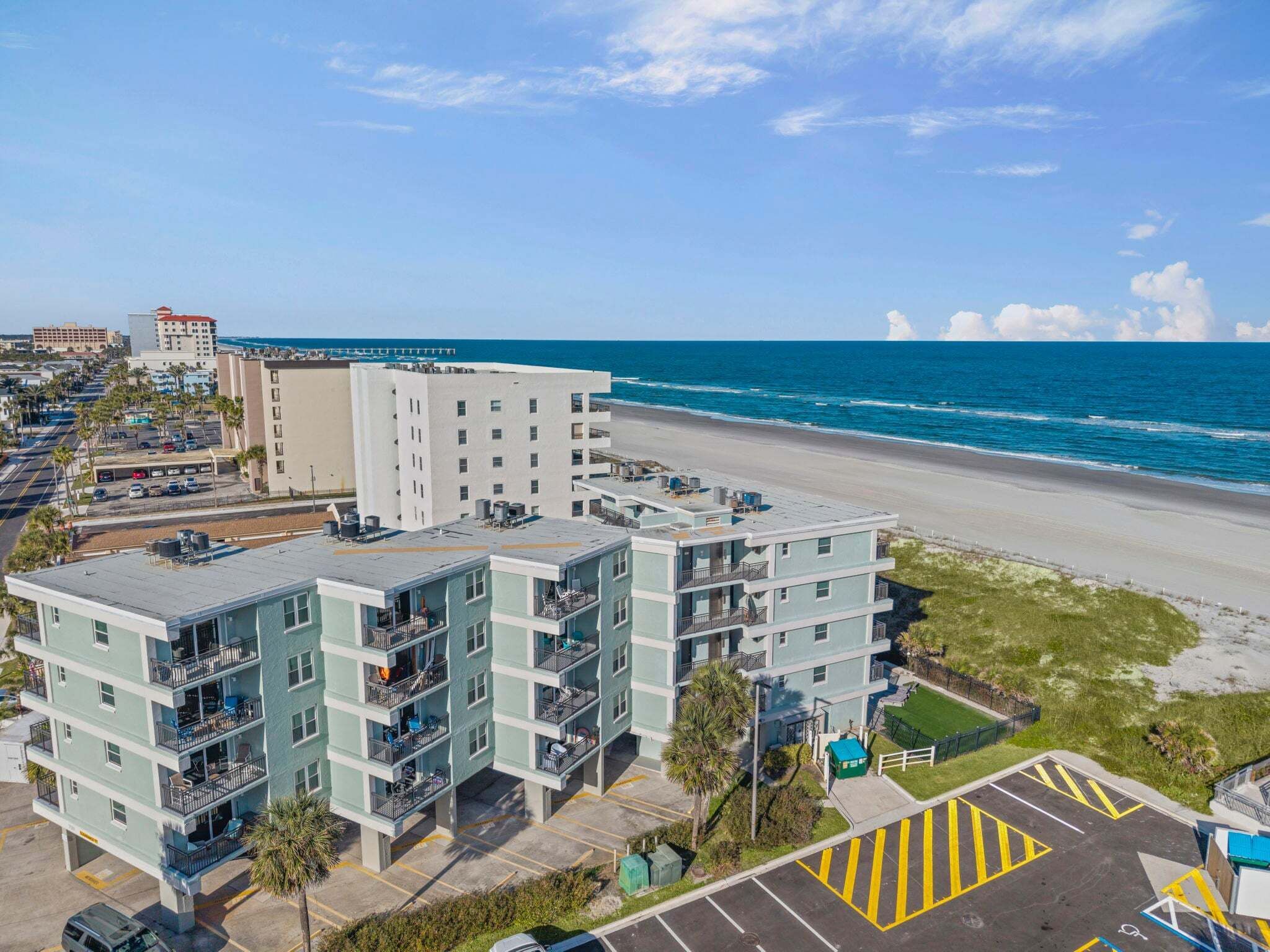 A multi-story hotel with balconies, a parking lot, and a beach view.