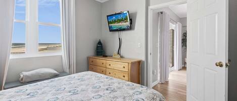 Un dormitorio con cama, televisión en la pared, cómoda y ventana con vista a la playa.