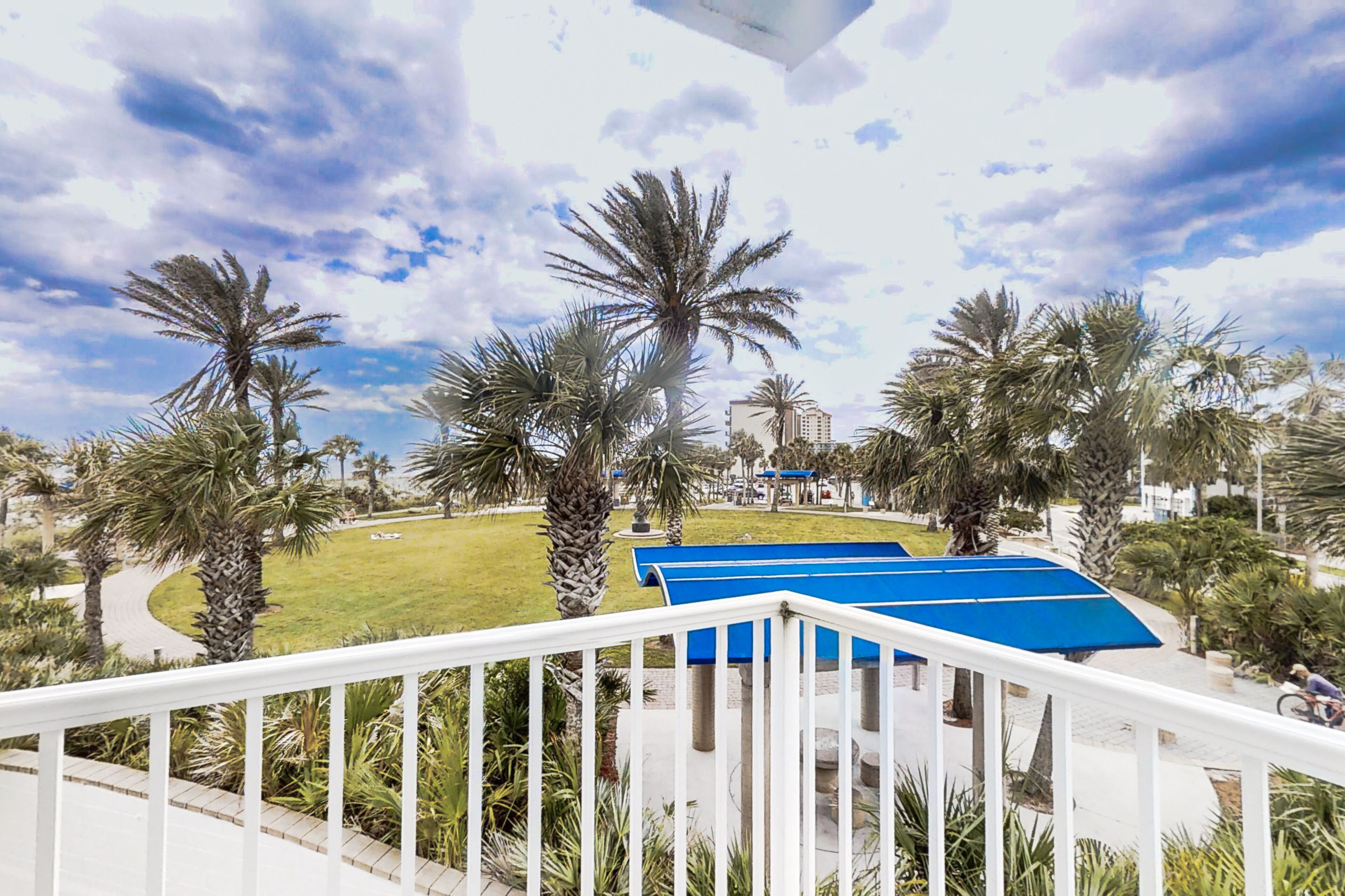 A view from a balcony overlooking a landscaped area with palm trees and a blue-roofed structure.